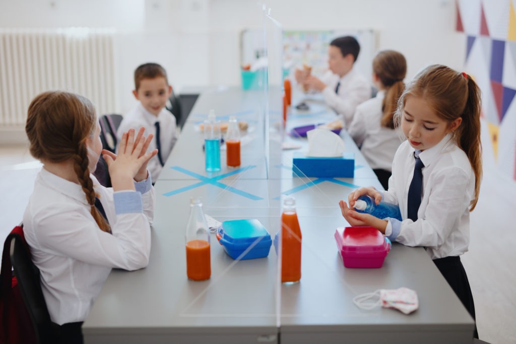 Group of schoolchildren eating lunch at their classroom with glass partition between them
