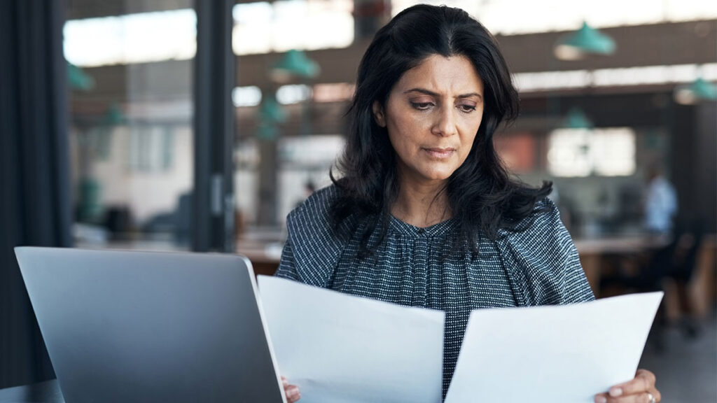 Shot of a mature businesswoman using a laptop and going through paperwork in a modern office